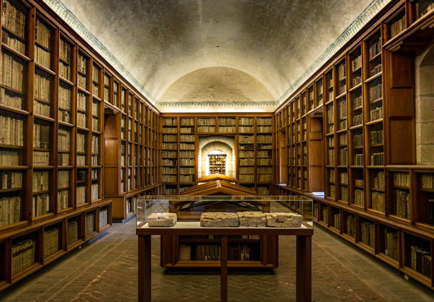 Old books fill shelves in a grand library hall with artifacts.